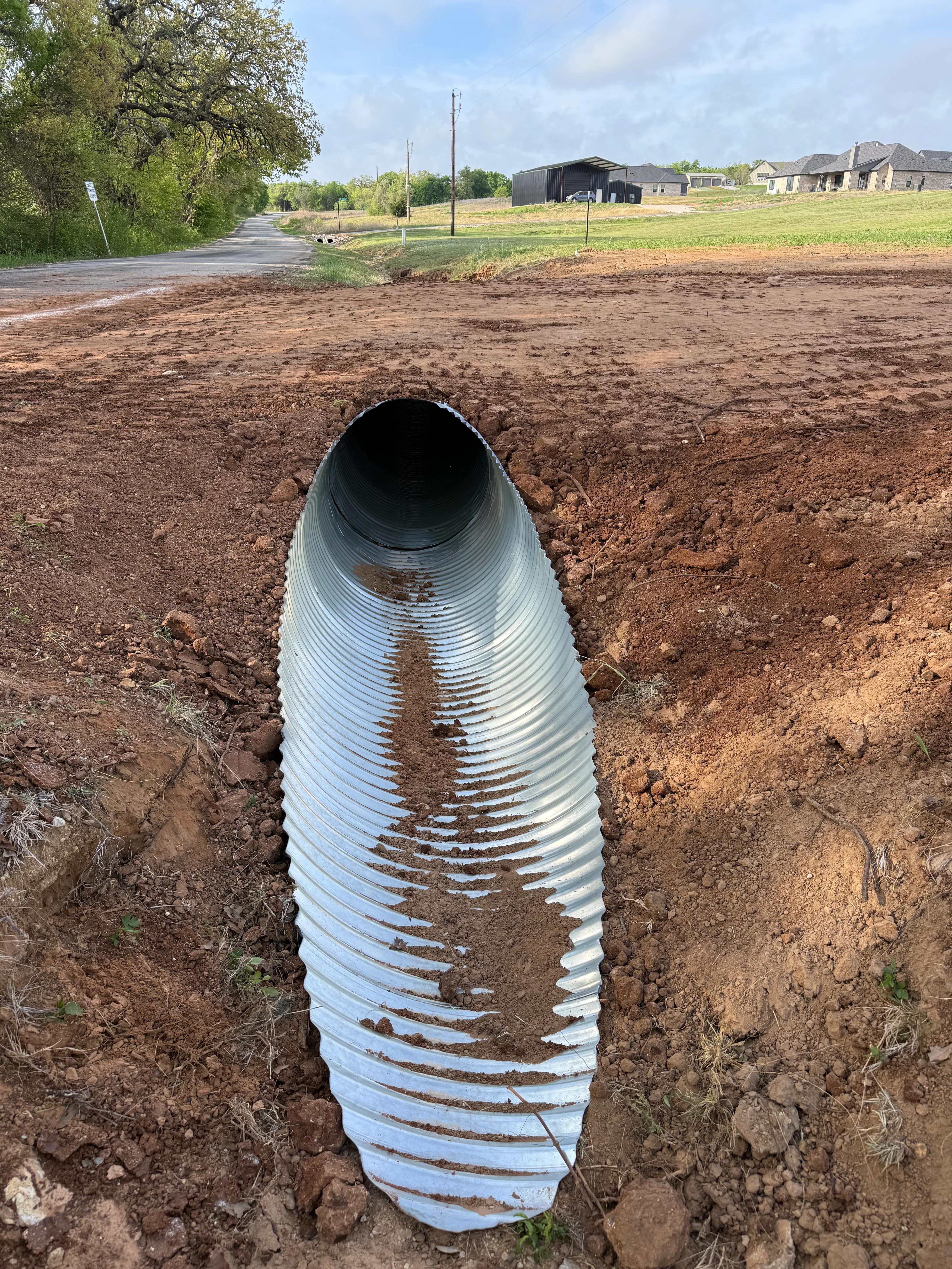 Corrugated metal drainage pipe installed in excavated trench with soil backfill