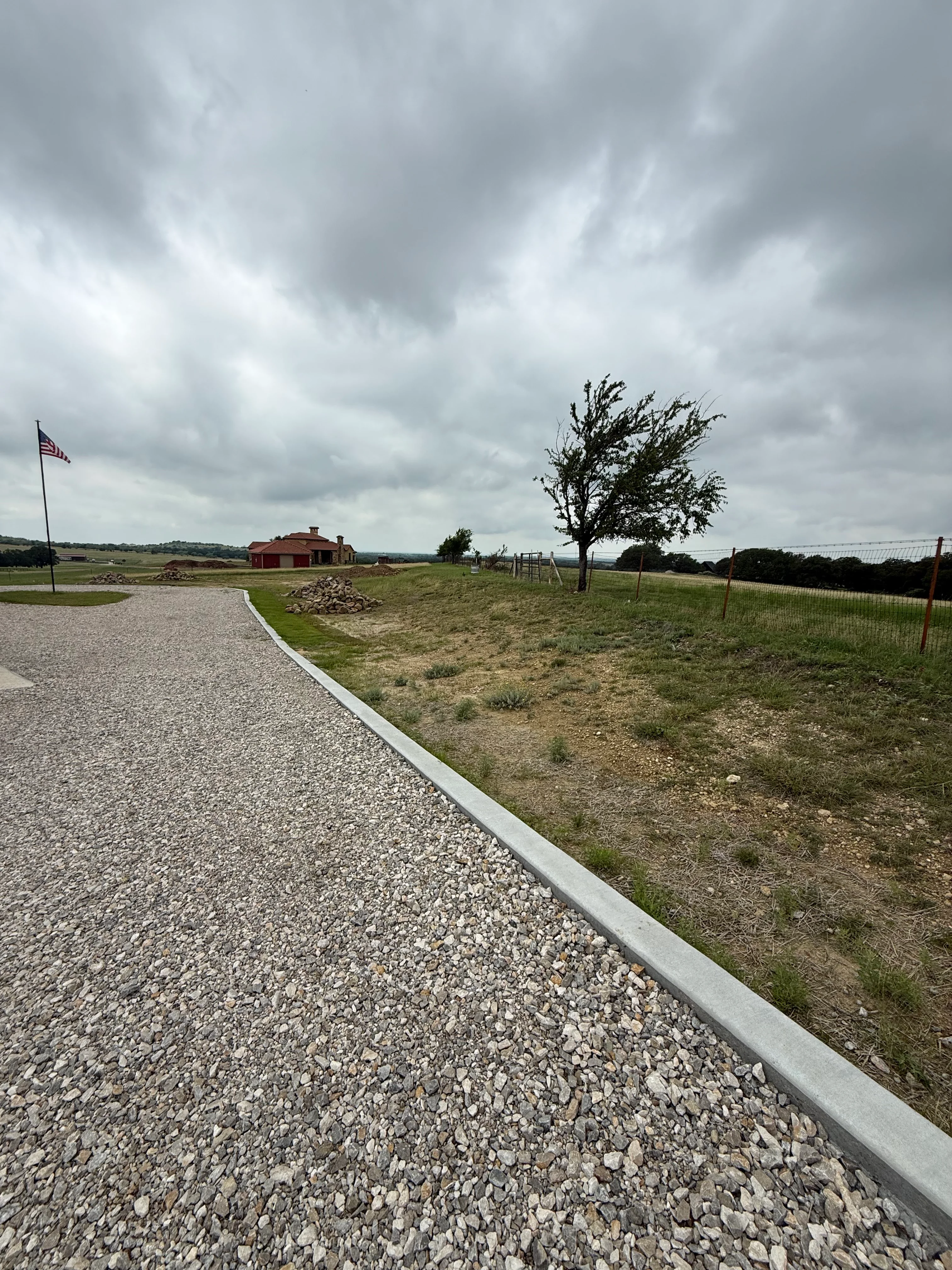 Gravel driveway with concrete edging leading to rural property with red barn