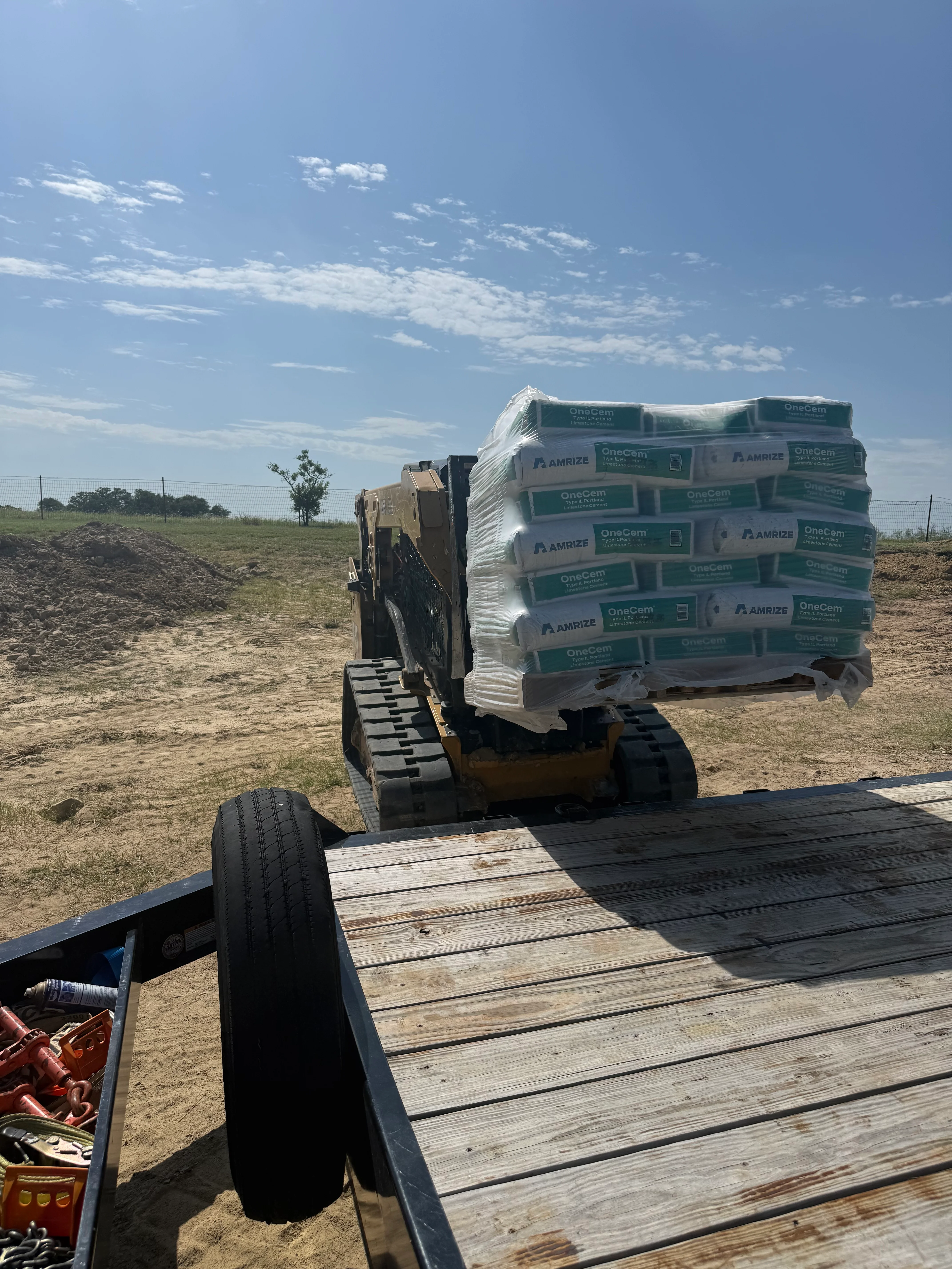 Compact track loader unloading palletized cement bags at rural job site
