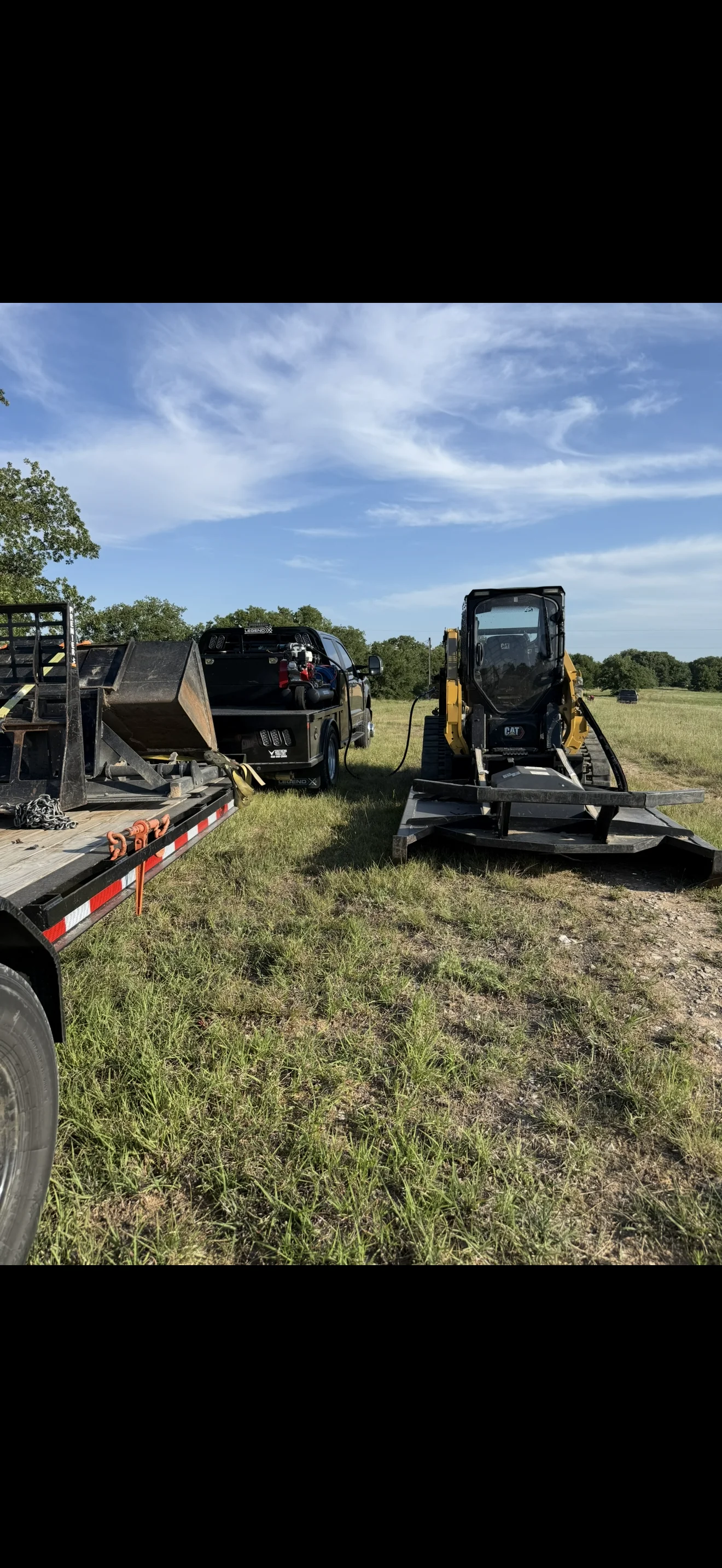 CAT skid steer loader on flatbed trailer with utility truck at Weatherford job site