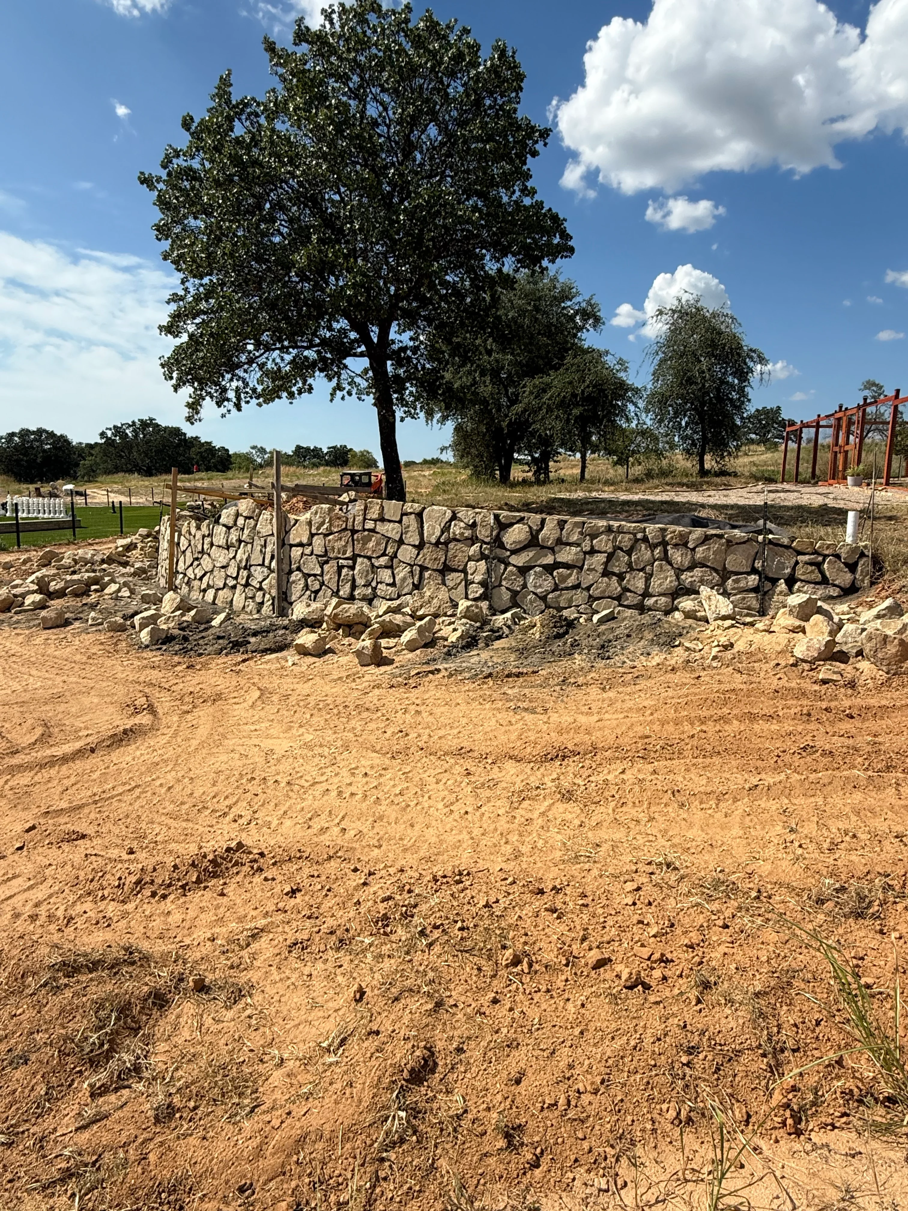 Dry-stacked stone retaining wall on rural property with mature oak trees