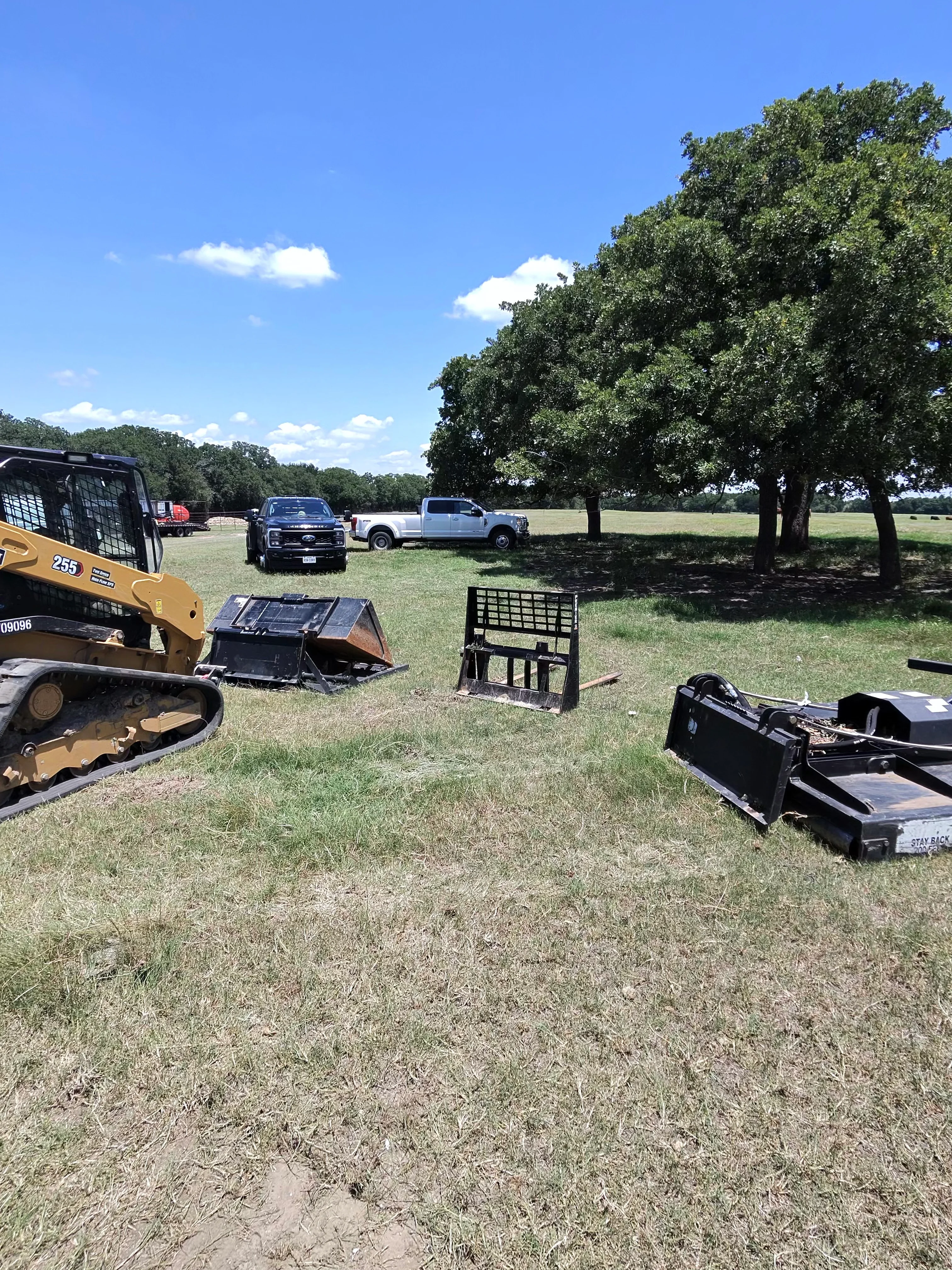 Excavation equipment including skid steer loader and attachments displayed on cleared land with service trucks