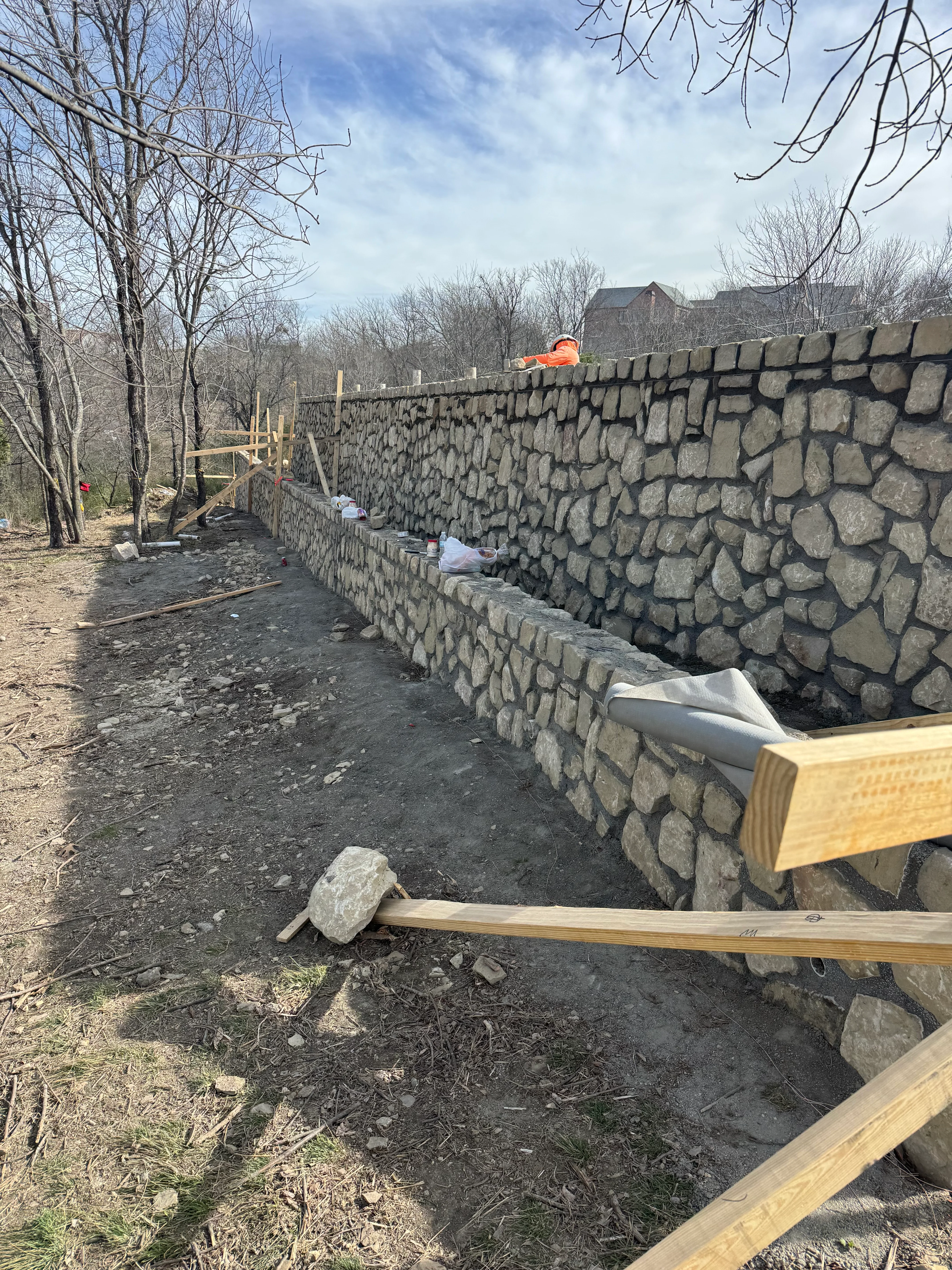 Stone retaining wall under construction with drainage pipe and wooden cap installation