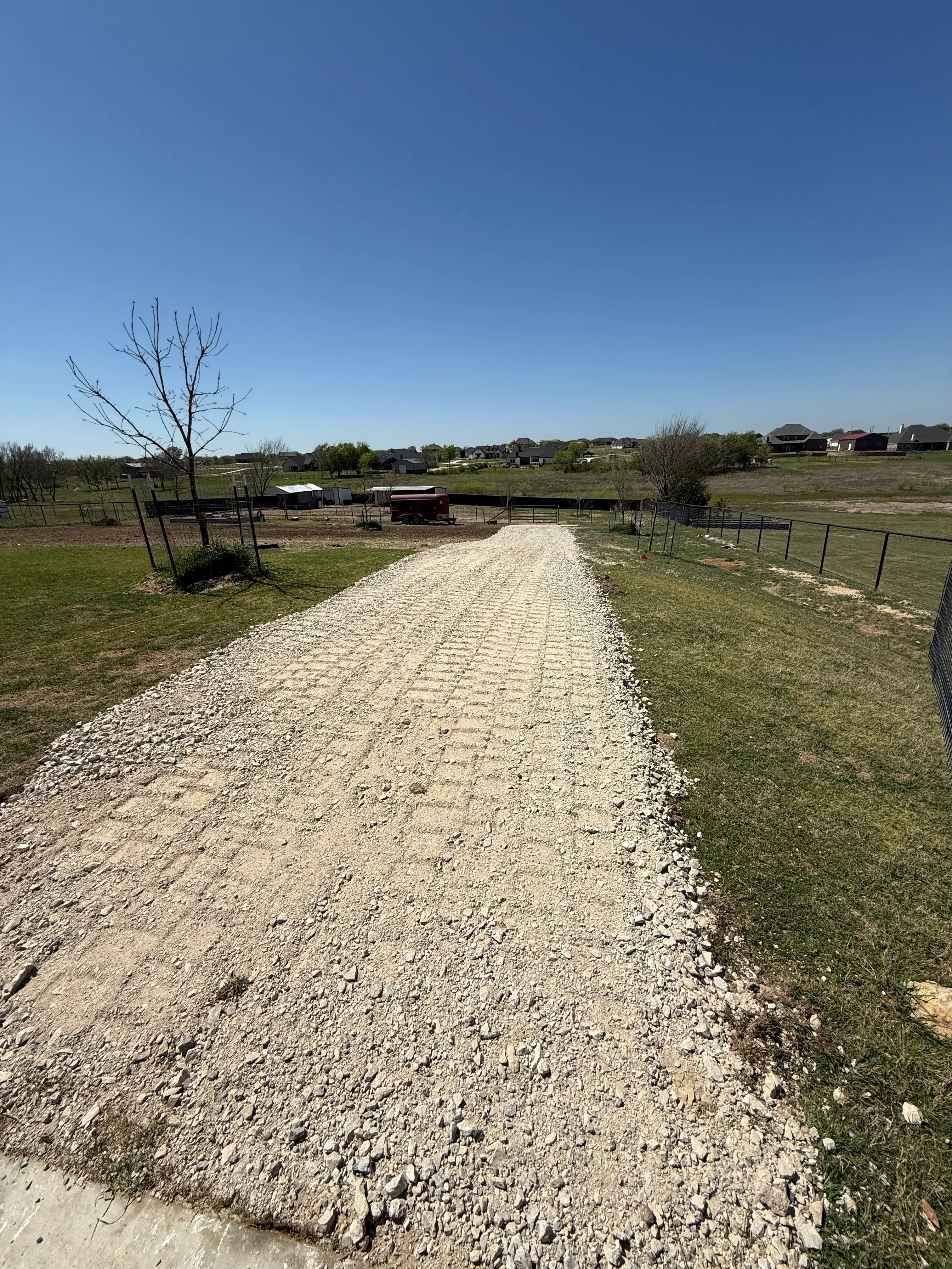 Newly installed gravel driveway on ranch property with metal fencing and green grass shoulders