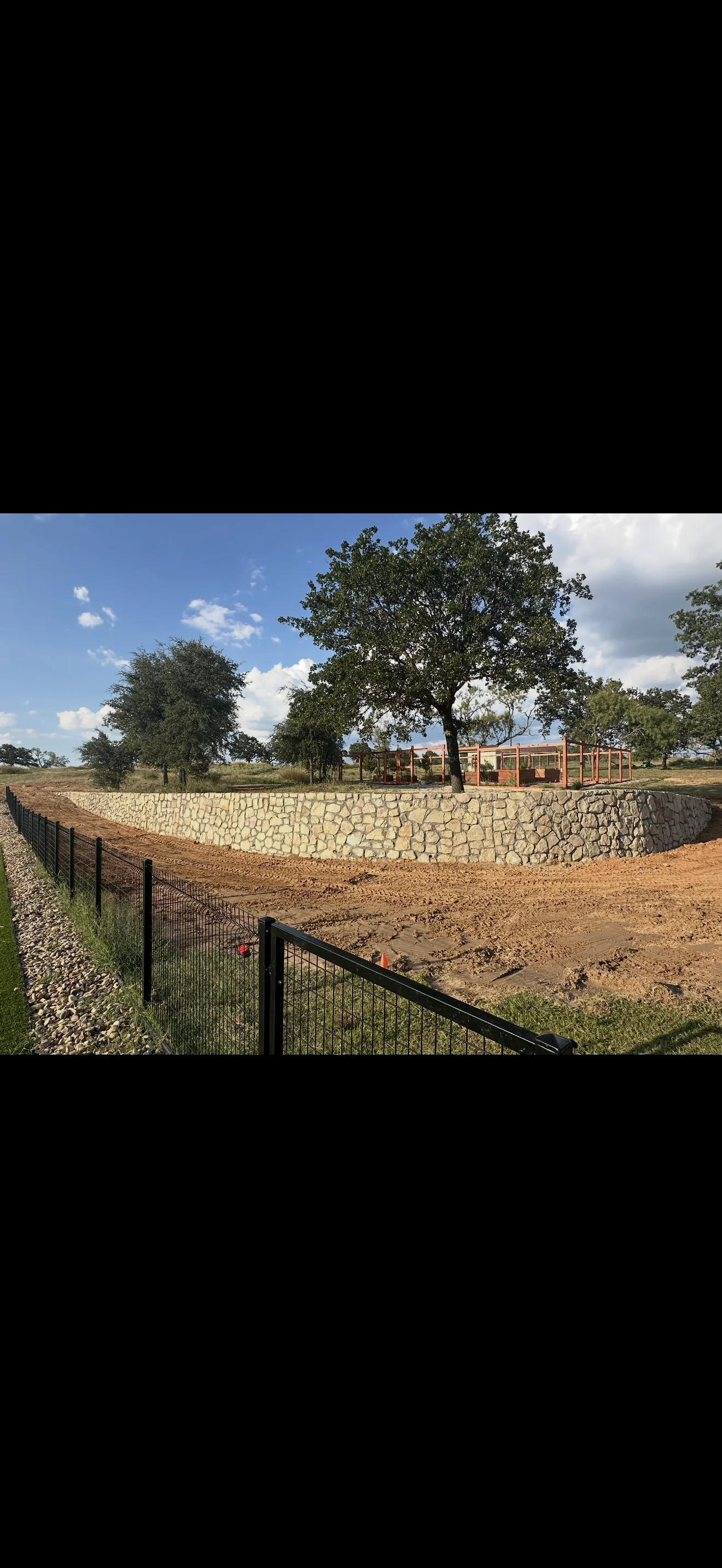Stone retaining wall with metal fencing and graded earthwork on rural property