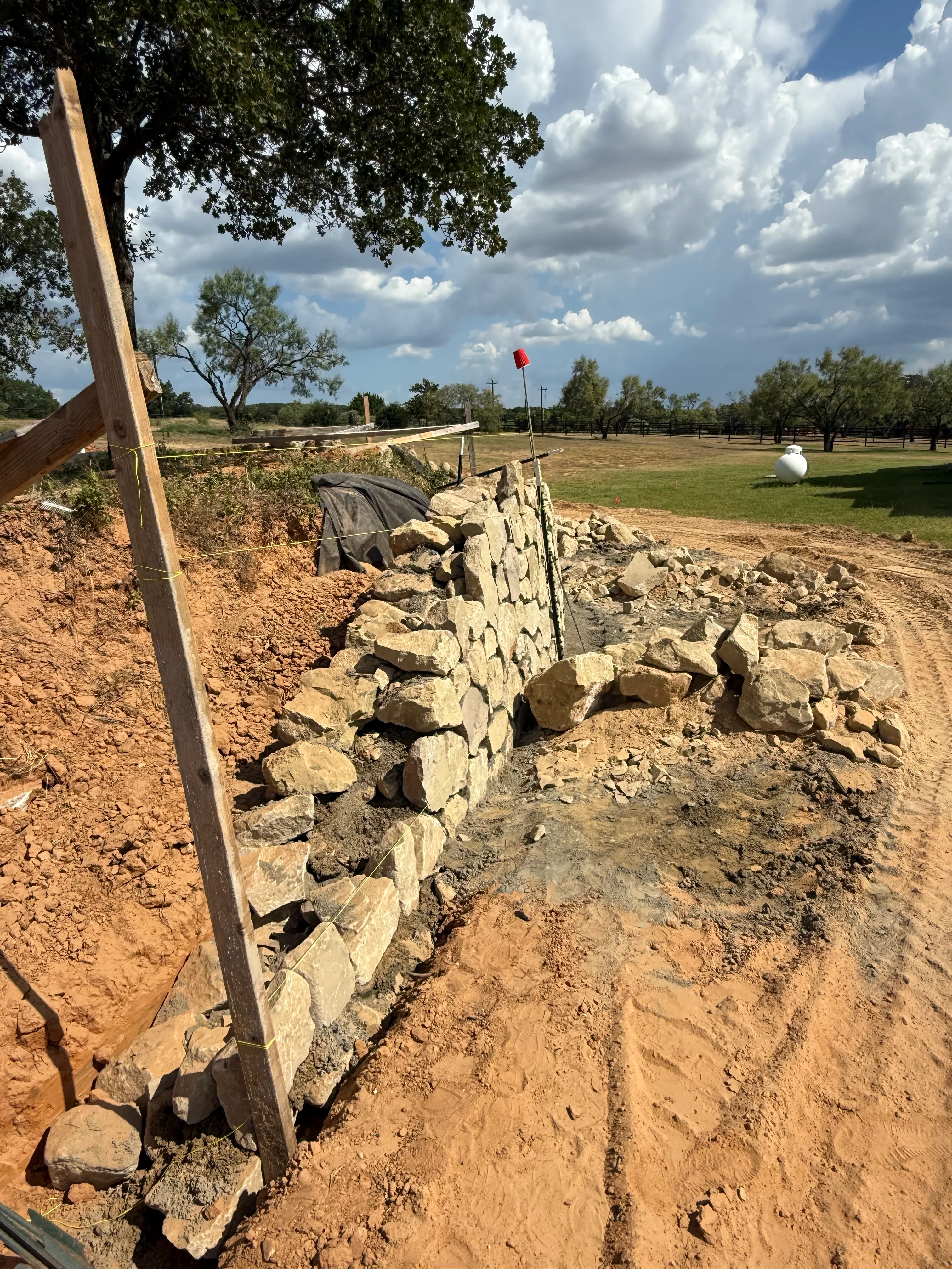 Stacked stone retaining wall with wooden support posts and geotextile backing during construction