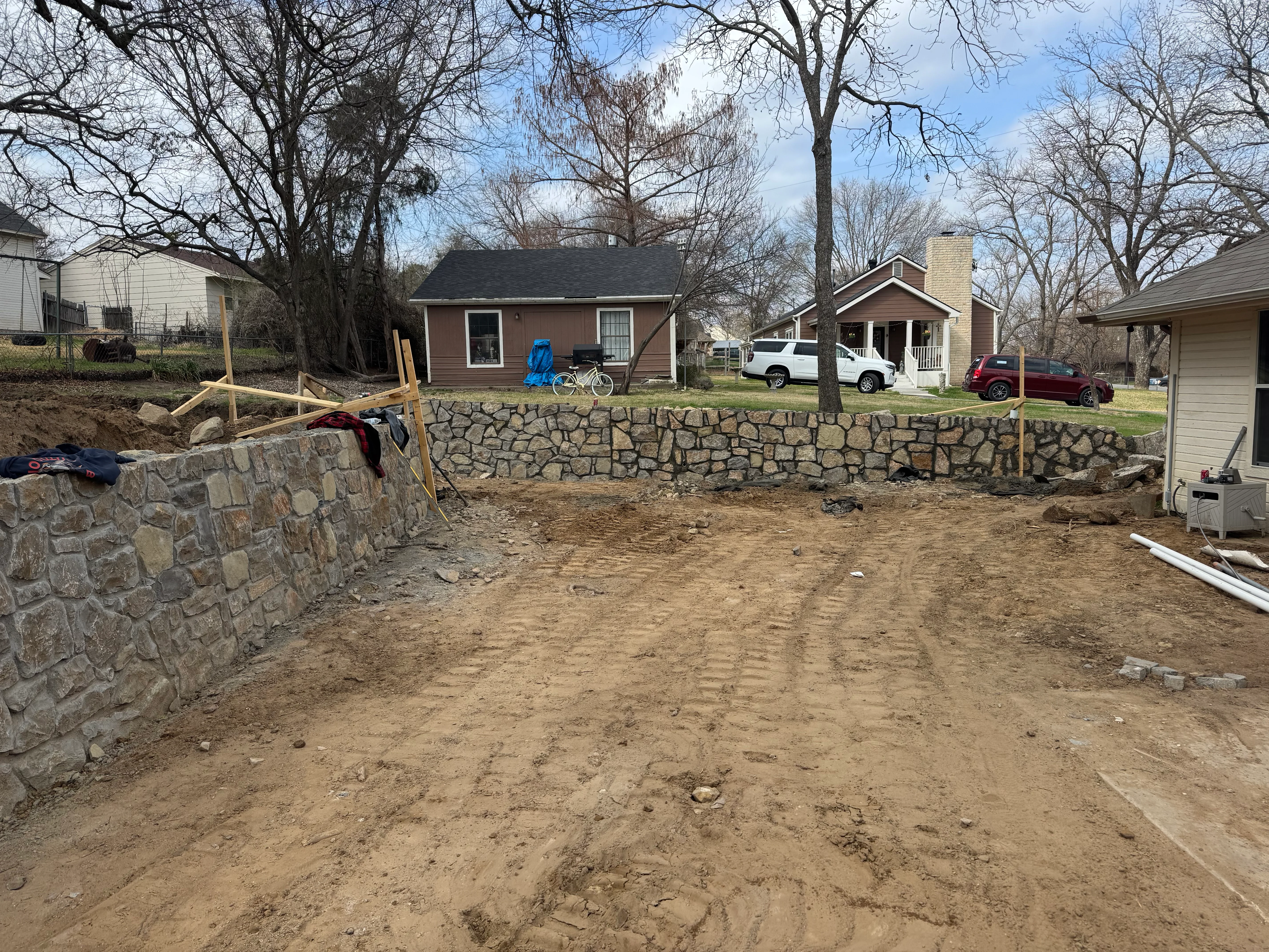 Stone retaining wall under construction with excavated dirt base and wooden bracing supports