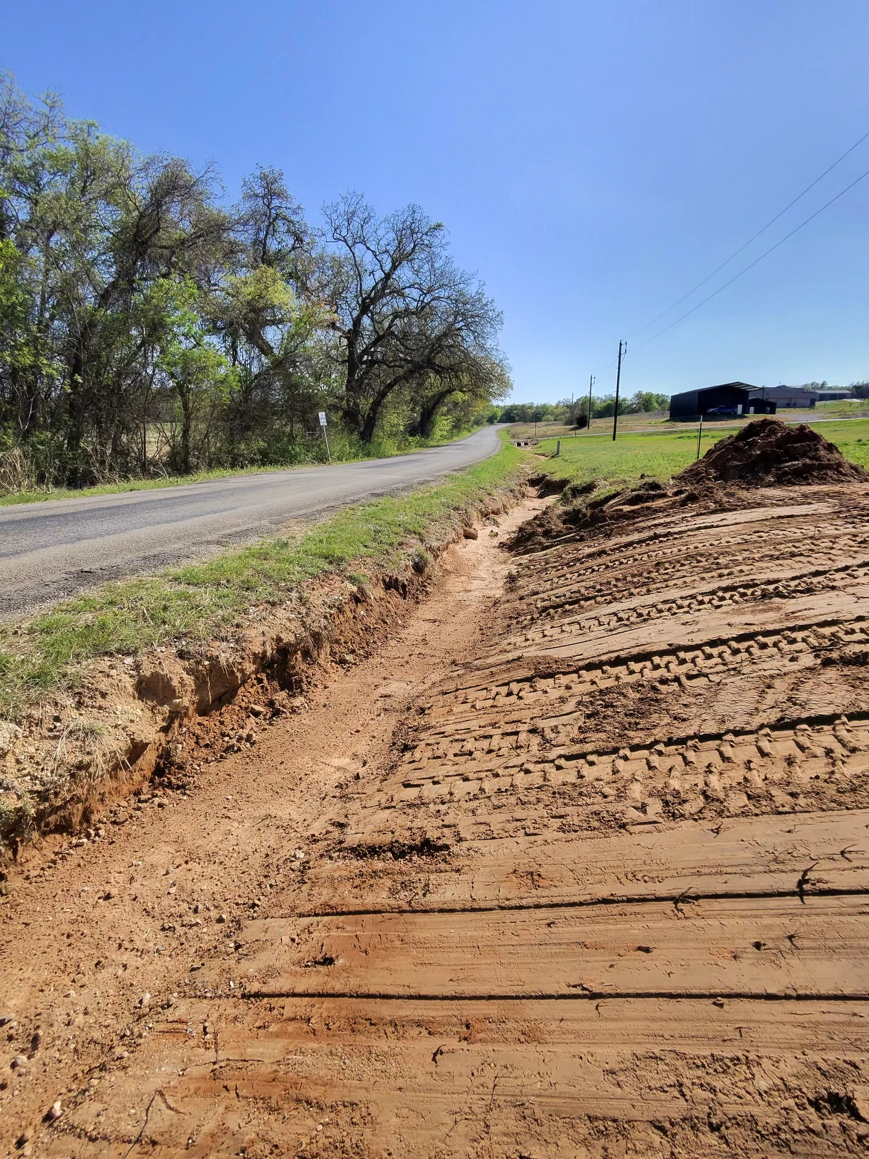 Excavated driveway entrance with graded soil, cut banks, and prepared base material along rural road