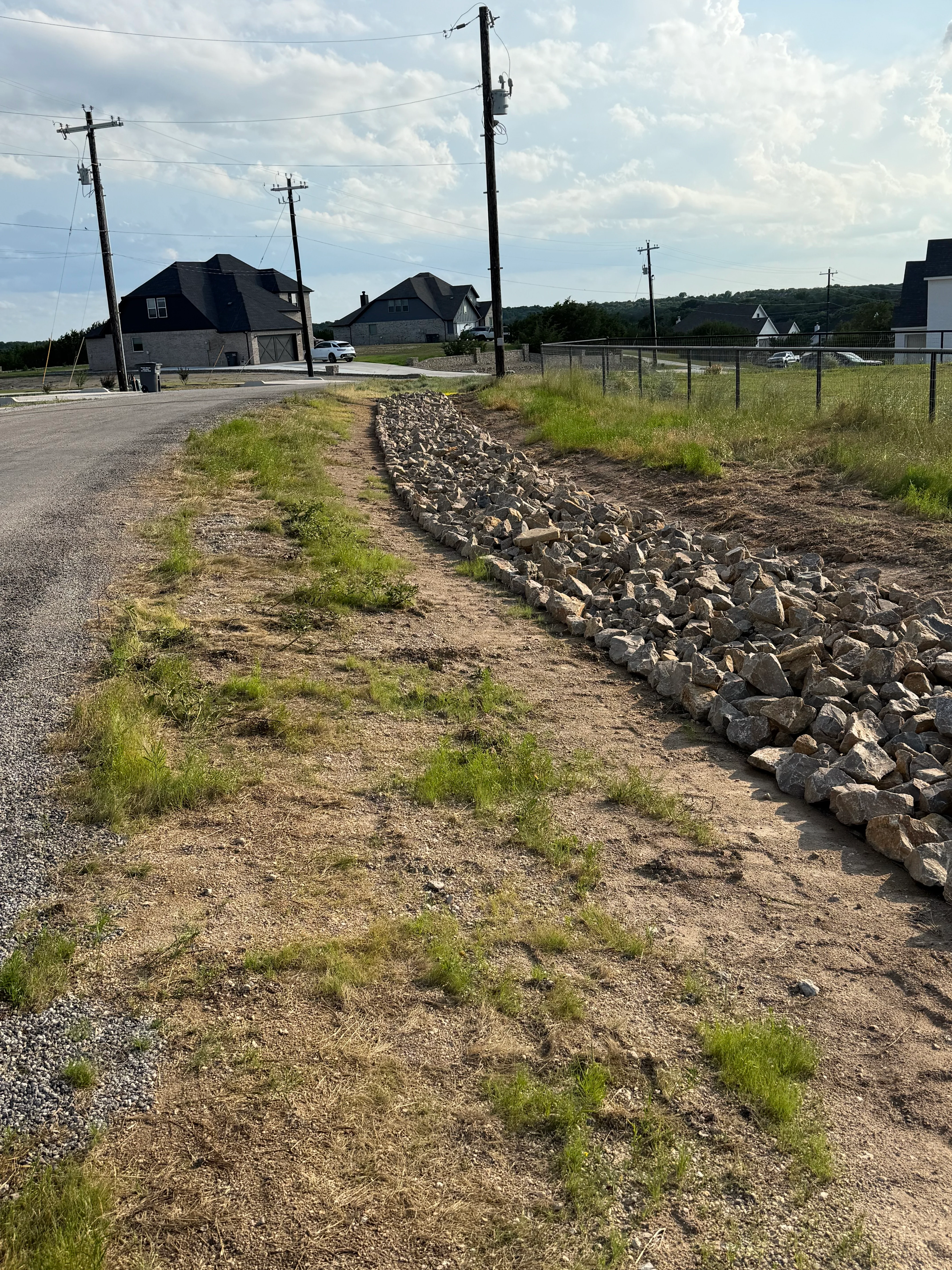 Rock-lined drainage swale along residential driveway with new home construction in background