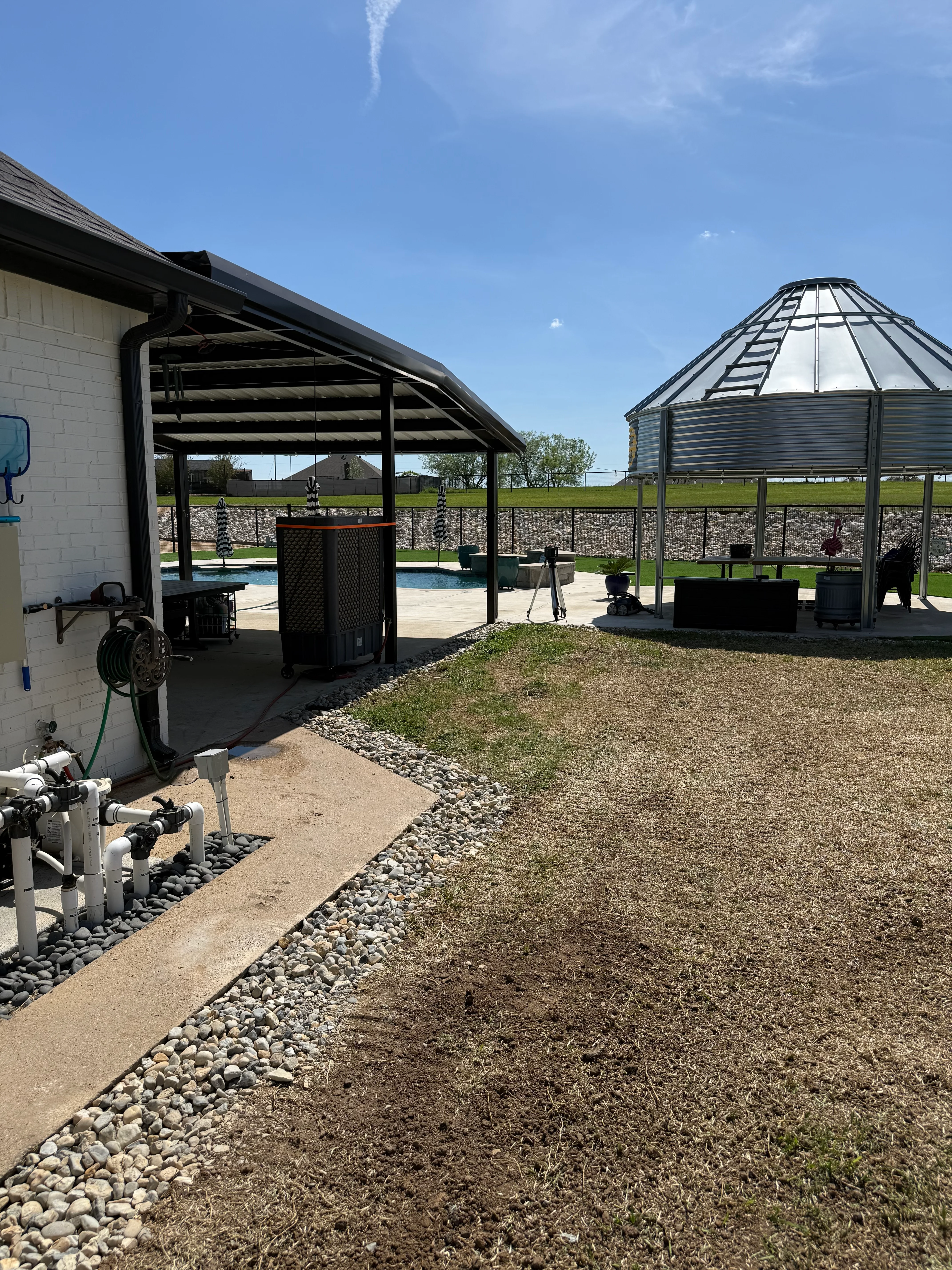 Completed pool area with concrete deck, metal pergola, grain bin shelter, and graded landscape