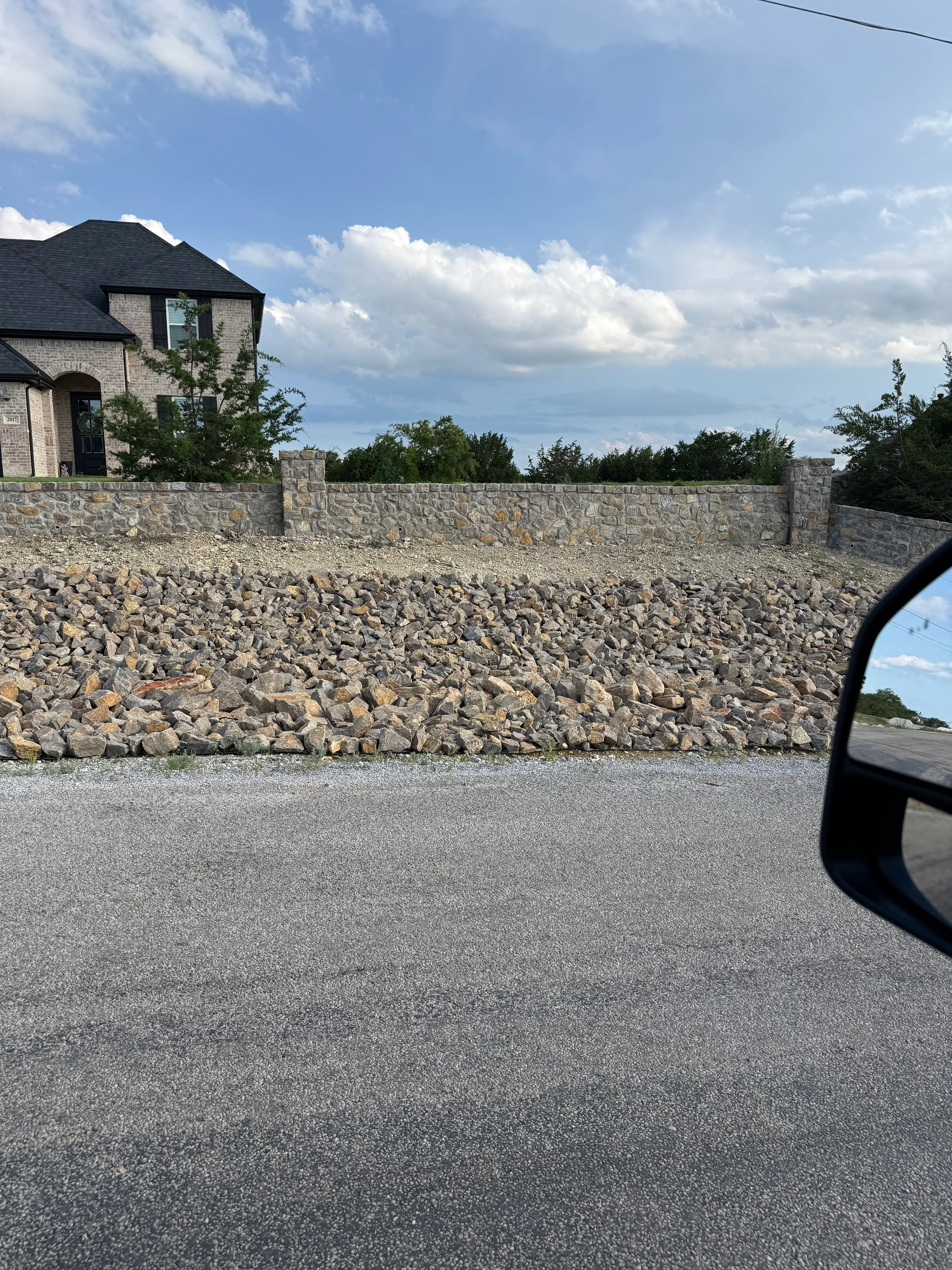 Stone retaining wall with asphalt driveway and brick home in background