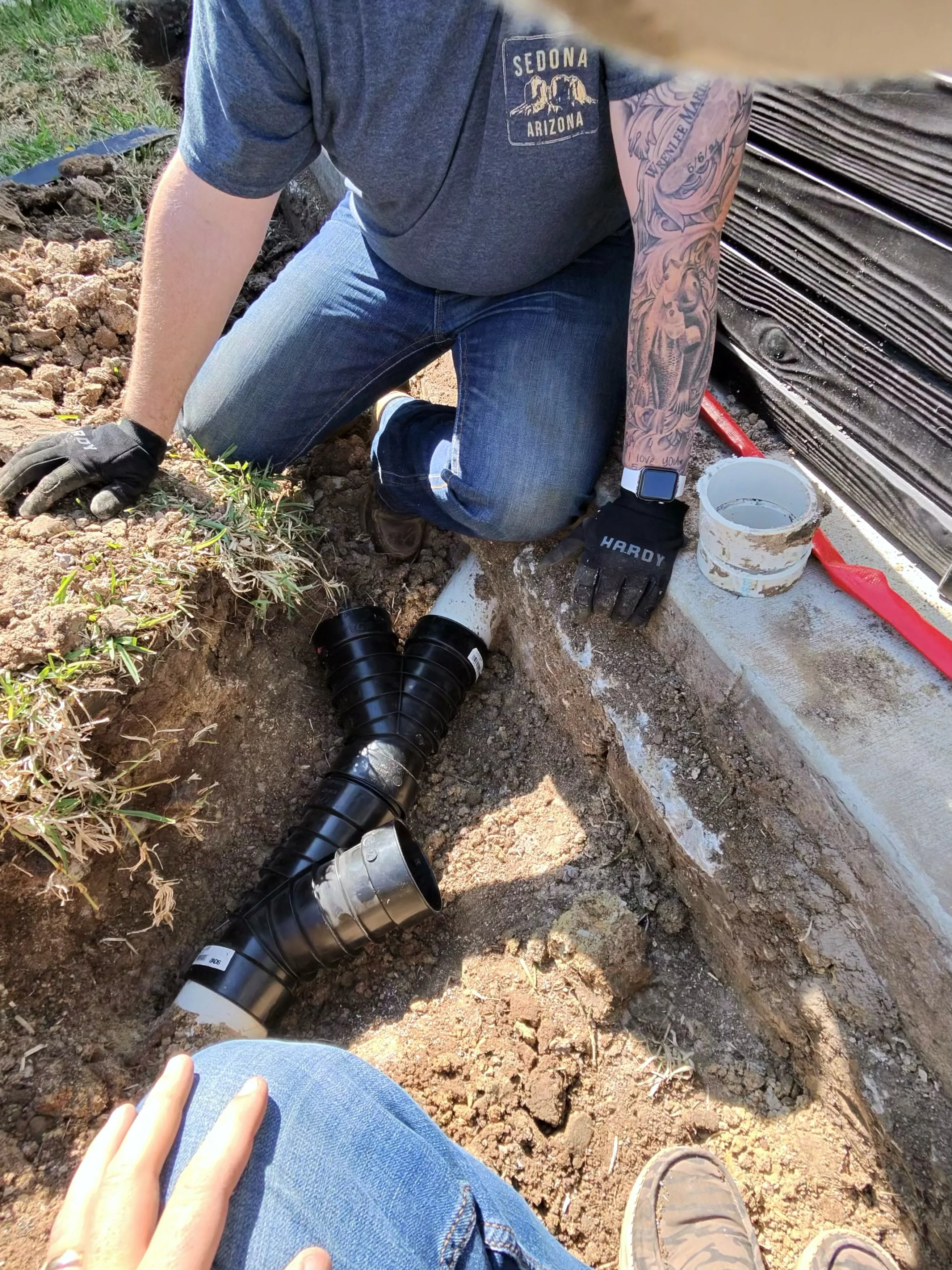 Drainage pipe installation in excavated trench with technician demonstrating proper placement and connections