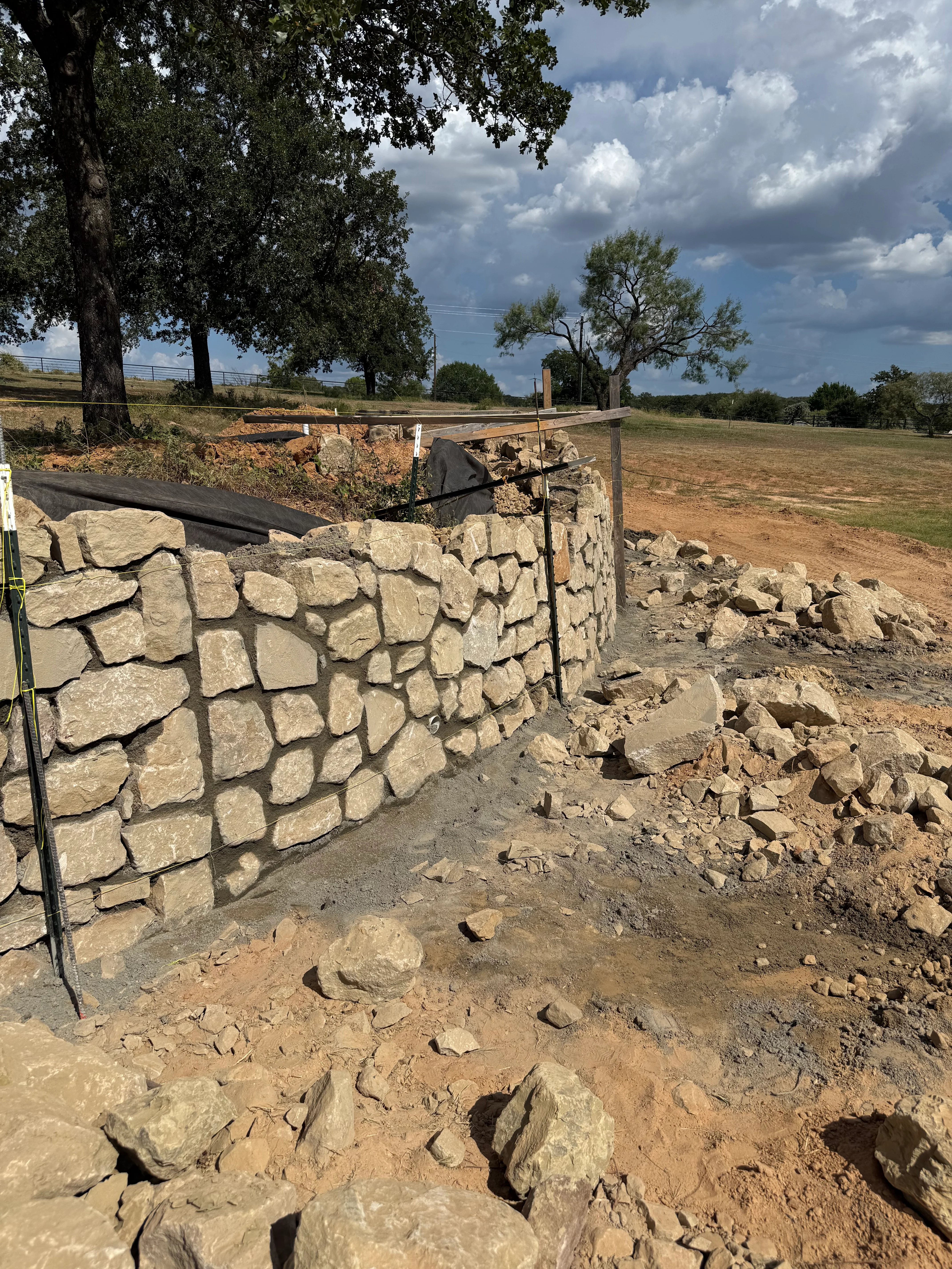 Completed limestone retaining wall on rural property with excavated base and surrounding landscape